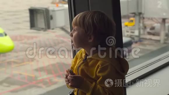 一个穿着黄色夹克的小男孩在机场的一扇大窗户前吃着饼干的慢镜头