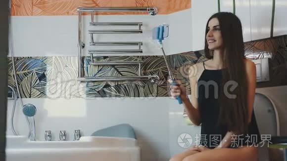 穿着黑色衬衫的漂亮女孩坐在马桶上在蓝色单脚架上自拍