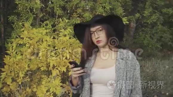 戴着黑色帽子和眼镜的年轻漂亮女人在户外使用智能手机