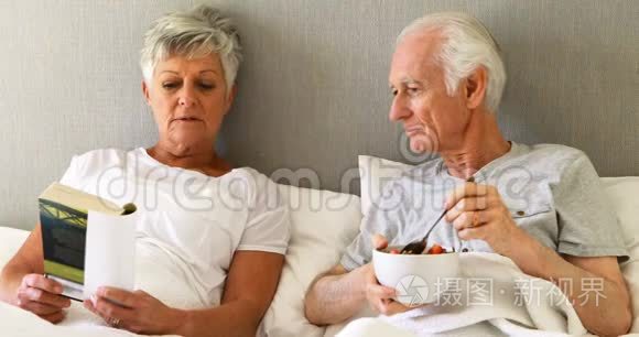 老人在床上一边吃早餐一边看书视频
