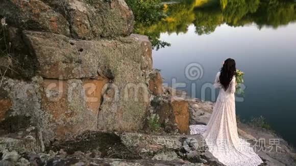年轻的新娘站在岩石河岸，日落