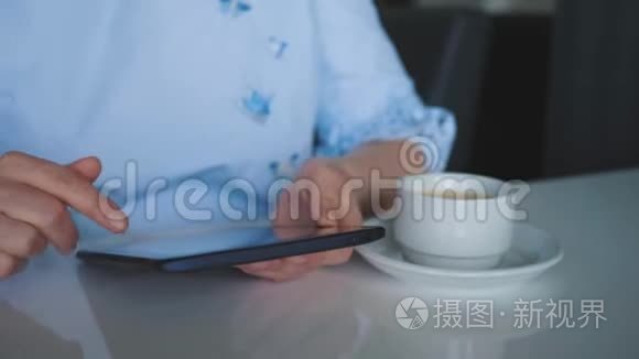 一个年轻的女孩坐在一张桌子旁，手里拿着一杯咖啡，一块数字平板电脑，翻阅着目录。