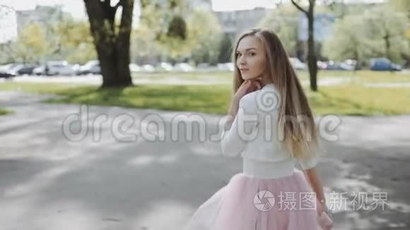 阳光明媚的一天，漂亮的年轻女人穿着粉红色的裙子，穿着白色的衬衫，在公园里戴着智能手机。 三轴