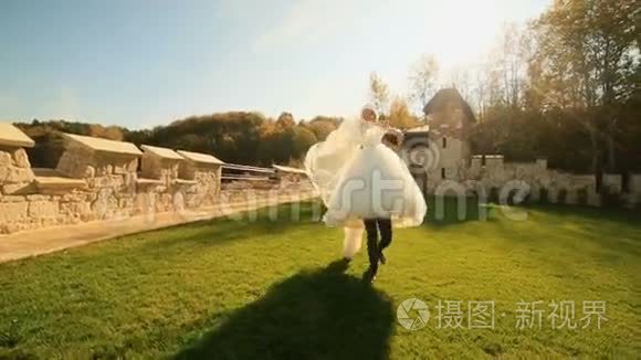快乐有趣的新郎牵着他迷人的新娘。 年轻的新婚夫妇在中世纪的城堡里一起玩