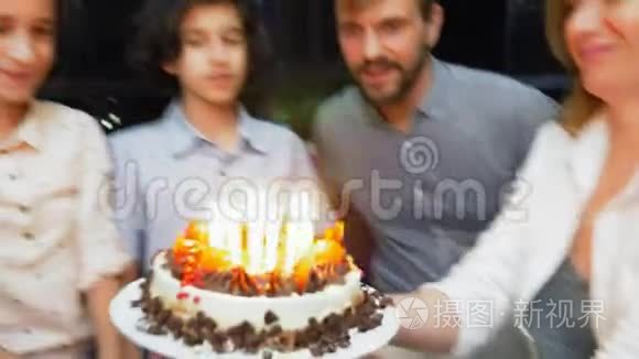 快乐的微笑男孩在她的生日蛋糕上吹蜡烛。 被家人包围的孩子。 有蜡烛的生日蛋糕