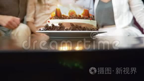 快乐的微笑男孩在她的生日蛋糕上吹蜡烛。 被家人包围的孩子。 有蜡烛的生日蛋糕