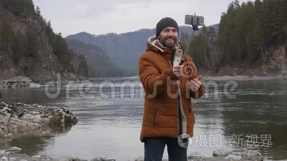 留胡子的游客在一条山河岸的手机上拍照。 慢动作