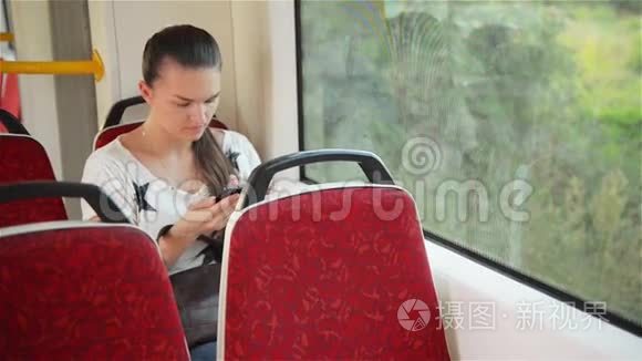 年轻女孩在乘坐公共汽车时使用智能手机，美丽的女人在城市交通中使用她的手机