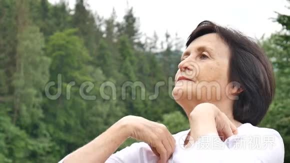 一位年长的女士在森林和山脉的外面为上臂做伸展运动