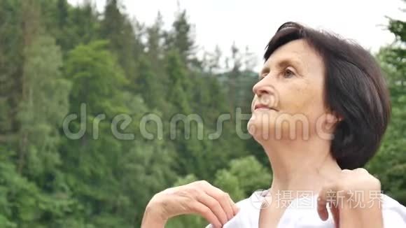 一位年长的女士在森林和山脉的外面为上臂做伸展运动