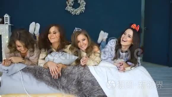 四个美丽的女孩躺在床上微笑。 女朋友在卧室里玩得开心
