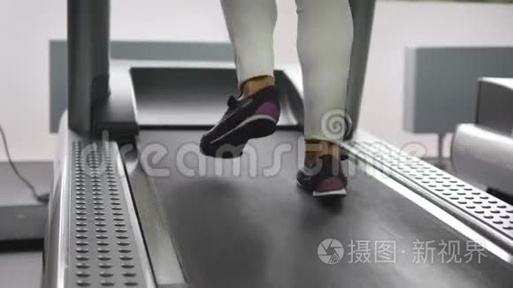 女性的腿在健身房的跑步机上行走和跑步。 年轻女性在有氧运动中锻炼。 女孩的脚