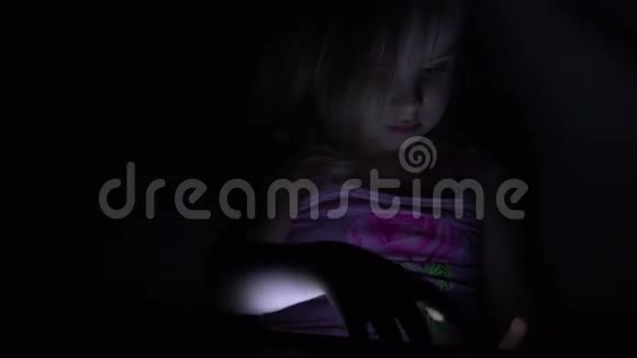 可爱的小女孩在黑暗房间的平板电脑上工作。 4K超高清，超高清视频的预览图