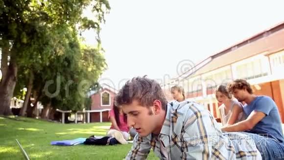 学生使用笔记本电脑，同学坐在草地后面