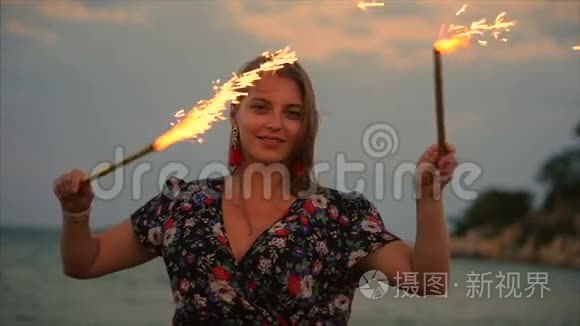 年轻快乐的微笑的女人，在日落时缓慢地用火花跳舞，在海滩上日落时用烟花。