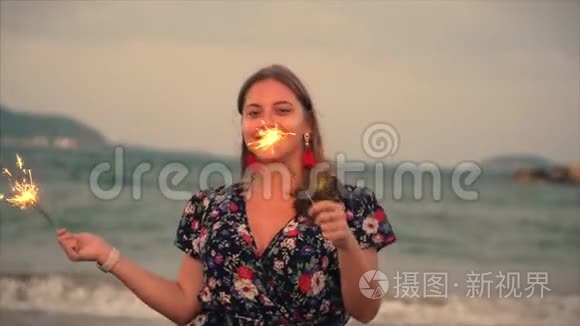 年轻快乐的微笑的女人，在日落时缓慢地用火花跳舞，在海滩上日落时用烟花。