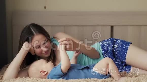 母亲和孩子在一张白色的床上。 妈妈和小男孩穿着尿布在阳光明媚的卧室里玩。 家长和小孩放松