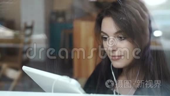 一位年轻女士在咖啡店用带耳机的平板电脑