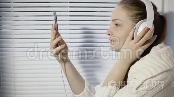 休息和放松，年轻的高加索女人坐在窗台上用智能手机用耳机听音乐