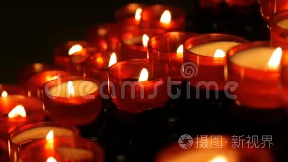 一排基督教祈祷红色的圆形蜡烛在黑暗中燃烧。 祈祷点燃蜡烛。 燃烧