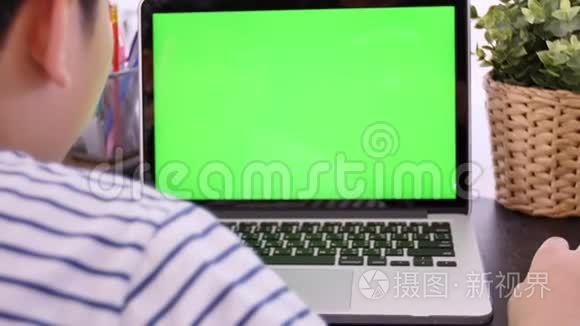 拍过肩膀的亚洲男孩看着绿色的屏幕。 办公室人员使用带有笔记本电脑绿色屏幕的笔记本电脑，