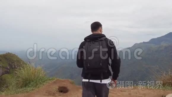 男性徒步旅行者到达山顶，伸出手臂向上。 带背包的年轻人站在边上