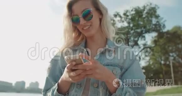 阳光明媚的一天，年轻的金发女人戴着太阳镜在城市里用手机。