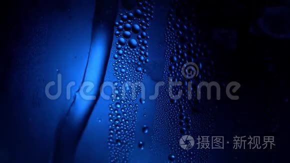 一滴水在一个玻璃特写宏观与闪闪发光的波克在蓝色模糊的背景。 抽象滴水。 雨滴