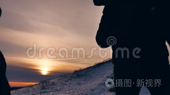 人们冬天剪影雪光.. 一群游客走在夕阳的剪影山上。 慢视频