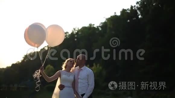 结婚那天的浪漫情侣。 新娘和新郎带着气球在夕阳的田野里。