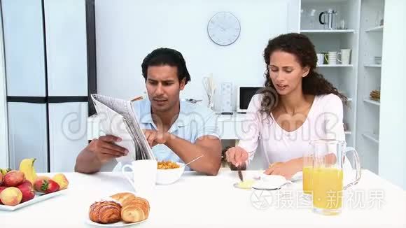 男人一边看报纸一边和女友吃早餐