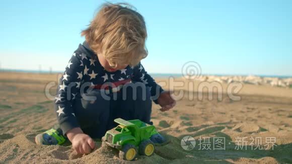 这个男孩正在海滩上玩一辆绿色的玩具自卸卡车。