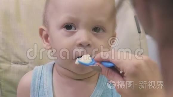 妈妈用勺子喂她的小儿子。 妈妈在家里给她可爱的孩子提供健康的食物。 快乐的小男孩