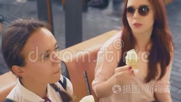 两个年轻的女人吃冰淇淋，坐在户外咖啡馆里，她们玩得很开心。 4K，慢动作，稳定。