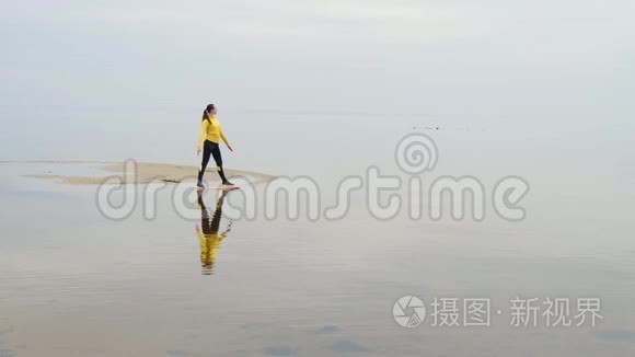 年轻苗条的女人在日落时在海边做健身瑜伽运动。 天与水的无缝自然背景