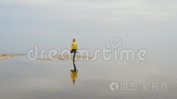 年轻苗条的女人在日落时在海边做健身瑜伽运动。 天与水的无缝自然背景