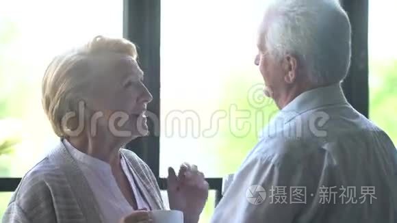 可爱快乐的老年夫妇在现代公寓。 他们说话，喝茶，笑