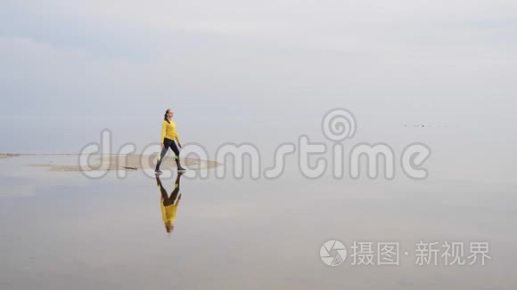 年轻苗条的女人在日落时在海边做健身瑜伽运动。 天与水的无缝自然背景