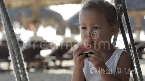 小可爱的小女孩坐在秋千上，在沙滩上吃红色的西瓜