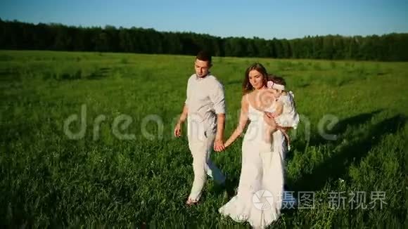 家庭幸福。 爸爸妈妈和一个小女孩，在夕阳下穿着白色衣服的田野里散步