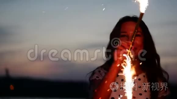 年轻快乐的微笑的女人，在日落时缓慢地用火花跳舞，在海滩上日落时用烟花。