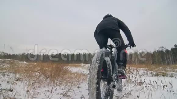 专业的极限运动运动员骑胖自行车在户外。 骑自行车在冬天的雪田，森林。 人类