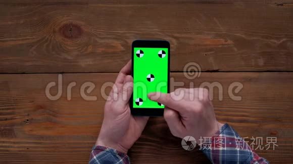 人使用智能手机，绿色屏幕在木桌上。