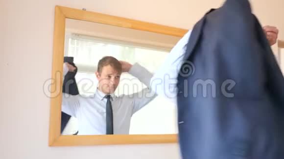 一个开朗可爱的男人在镜子前穿衣服，对着镜子微笑。 4k，慢动作视频的预览图