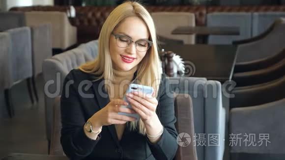 一个金发商务女性，穿着西装，拿着电话坐在咖啡馆的桌子旁