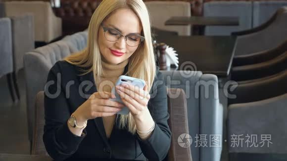 一个金发商务女性，穿着西装，拿着电话坐在咖啡馆的桌子旁