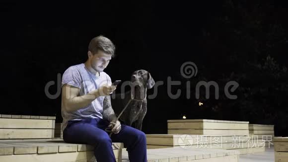 一个金发美女和他的狗在夜间公园的长椅上冲浪