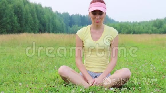美丽的女孩坐在绿色的草地上，在夏天的晚上冥想