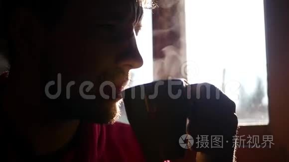 一个长着浓密胡须的男人，坐在窗户对面，喝着美味的热黑咖啡，动作缓慢