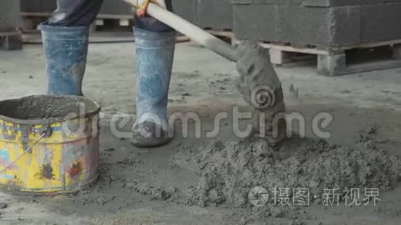 工人铲拌混凝土，并在施工现场放入桶中。